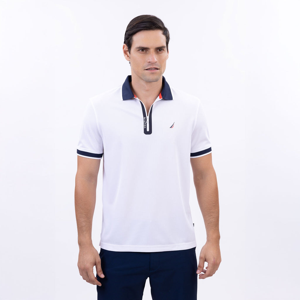 Hombre usando polo blanca con cierre, cuello azul marino y logo Nautica, hecha con poliéster reciclado