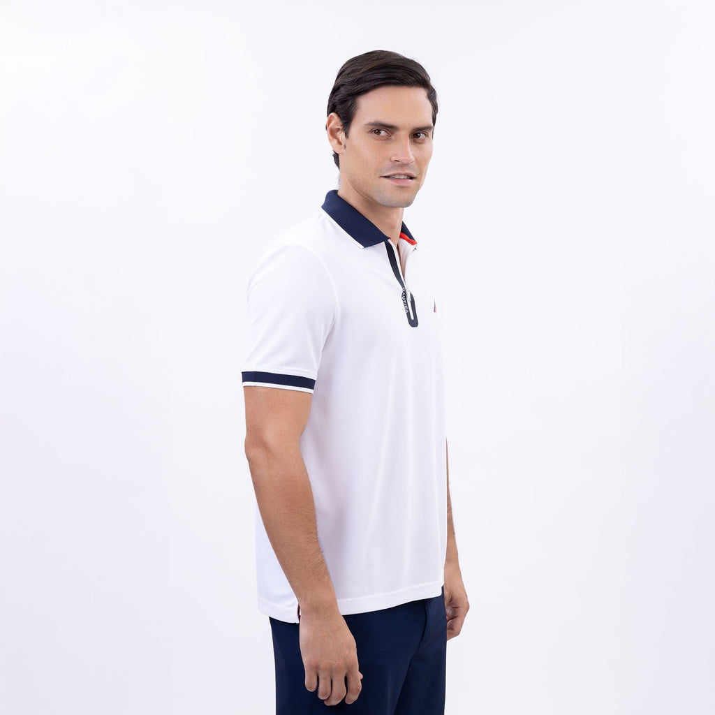 Hombre usando polo blanca con cierre, cuello azul marino y logo Nautica, hecha con poliéster reciclado