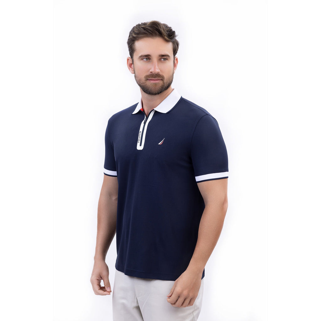 Hombre usando polo azul marino con cierre, cuello blanco y logo Nautica, hecha con poliéster reciclado
