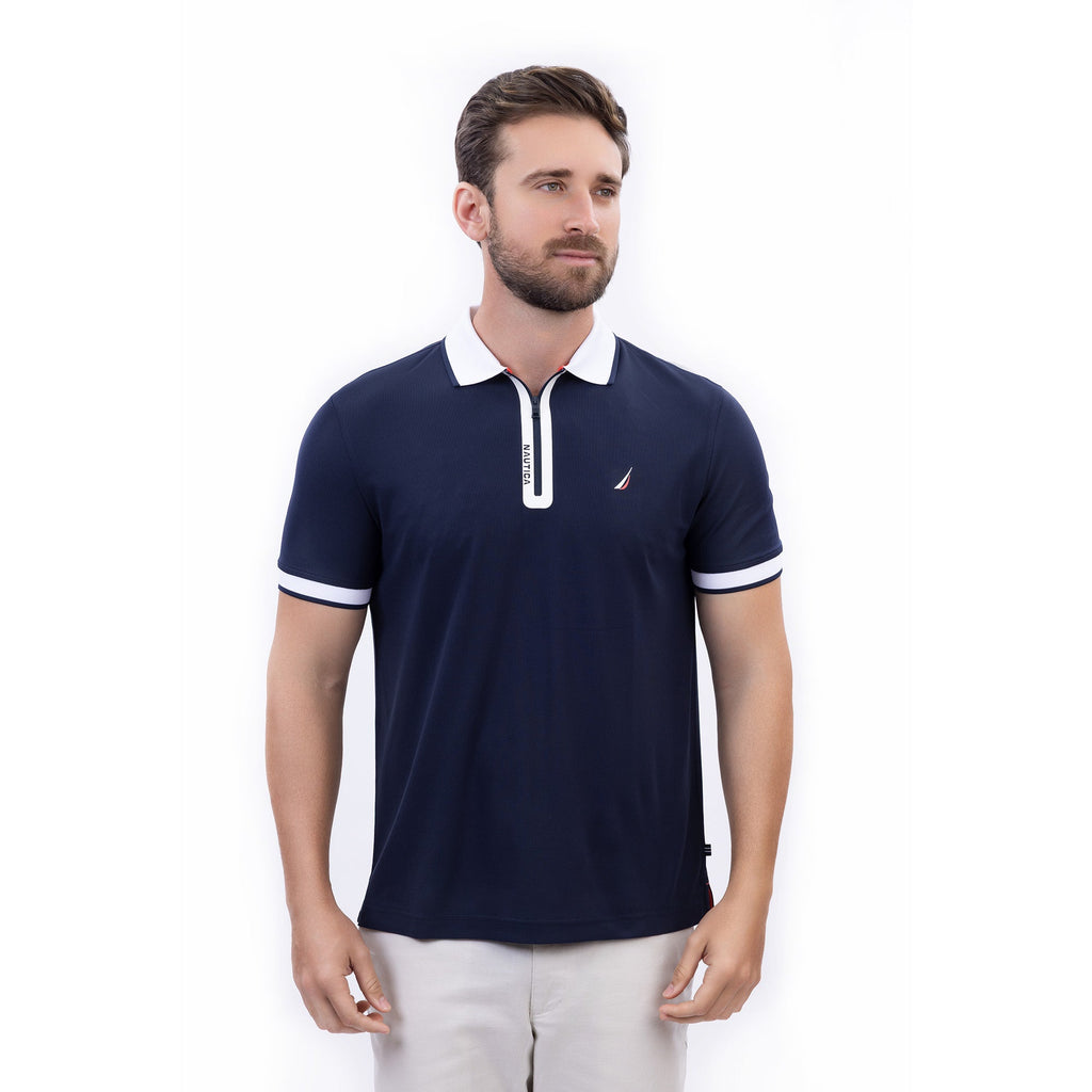 Hombre usando polo azul marino con cierre, cuello blanco y logo Nautica, hecha con poliéster reciclado