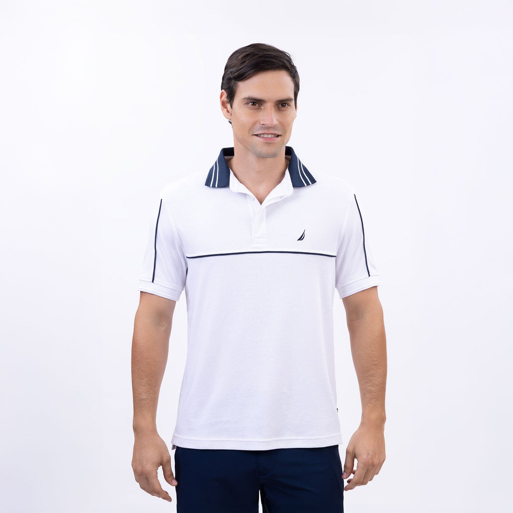 Hombre usando polo blanca con vivos azul marino y logo Nautica bordado, estilo náutico casual
