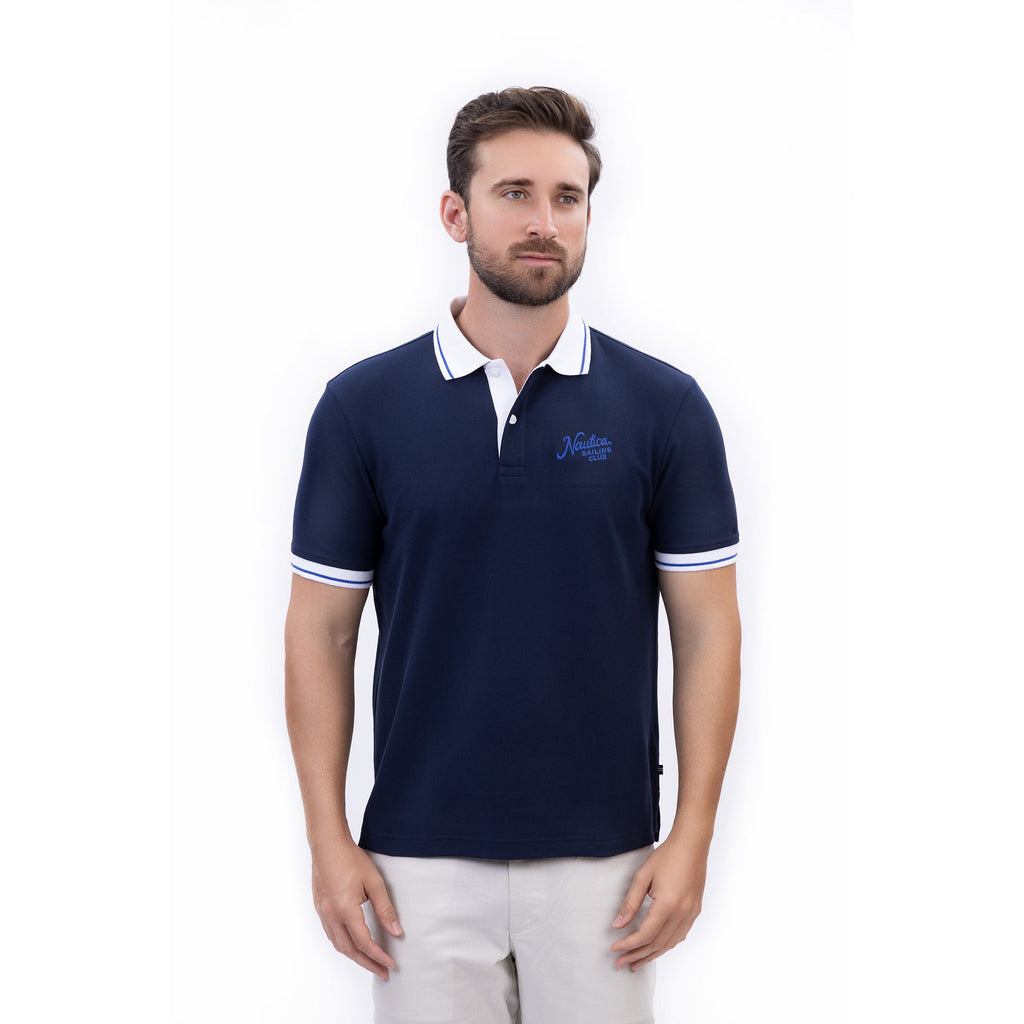 Hombre usando polo azul marino con cuello blanco y logo Nautica, estilo clásico náutico